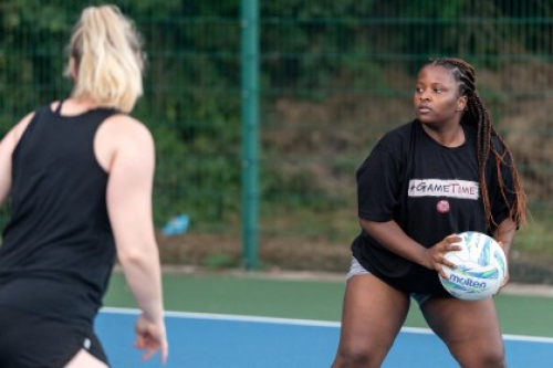 A woman holds a netball on an outside court as an opponent closes in.