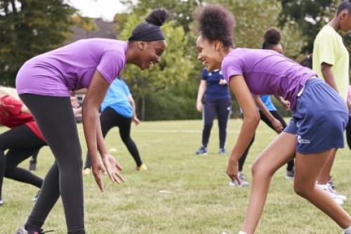 Two girls face other on a field, both leaning forwards in a wrestling stance.
