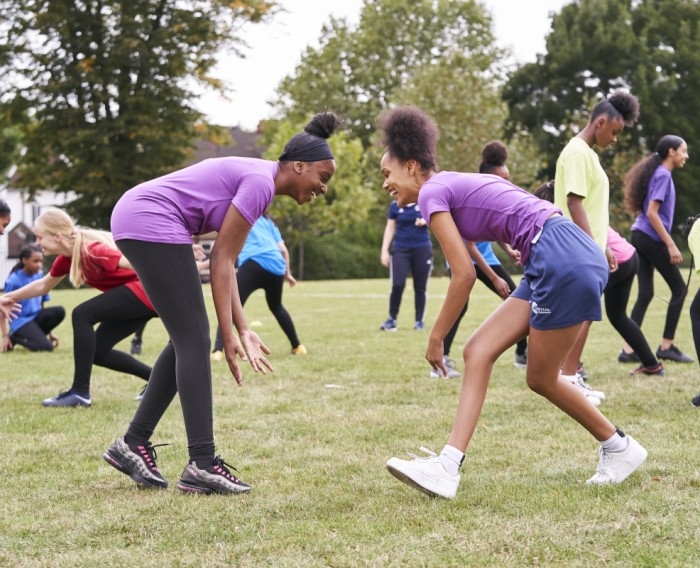 Two girls face other on a field, both leaning forwards in a wrestling stance.
