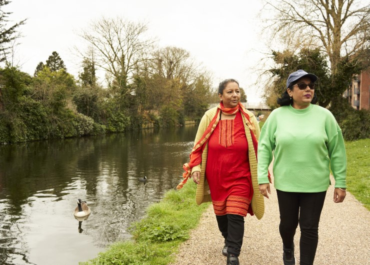 Two women walk side-by-side on a path beside a canal.