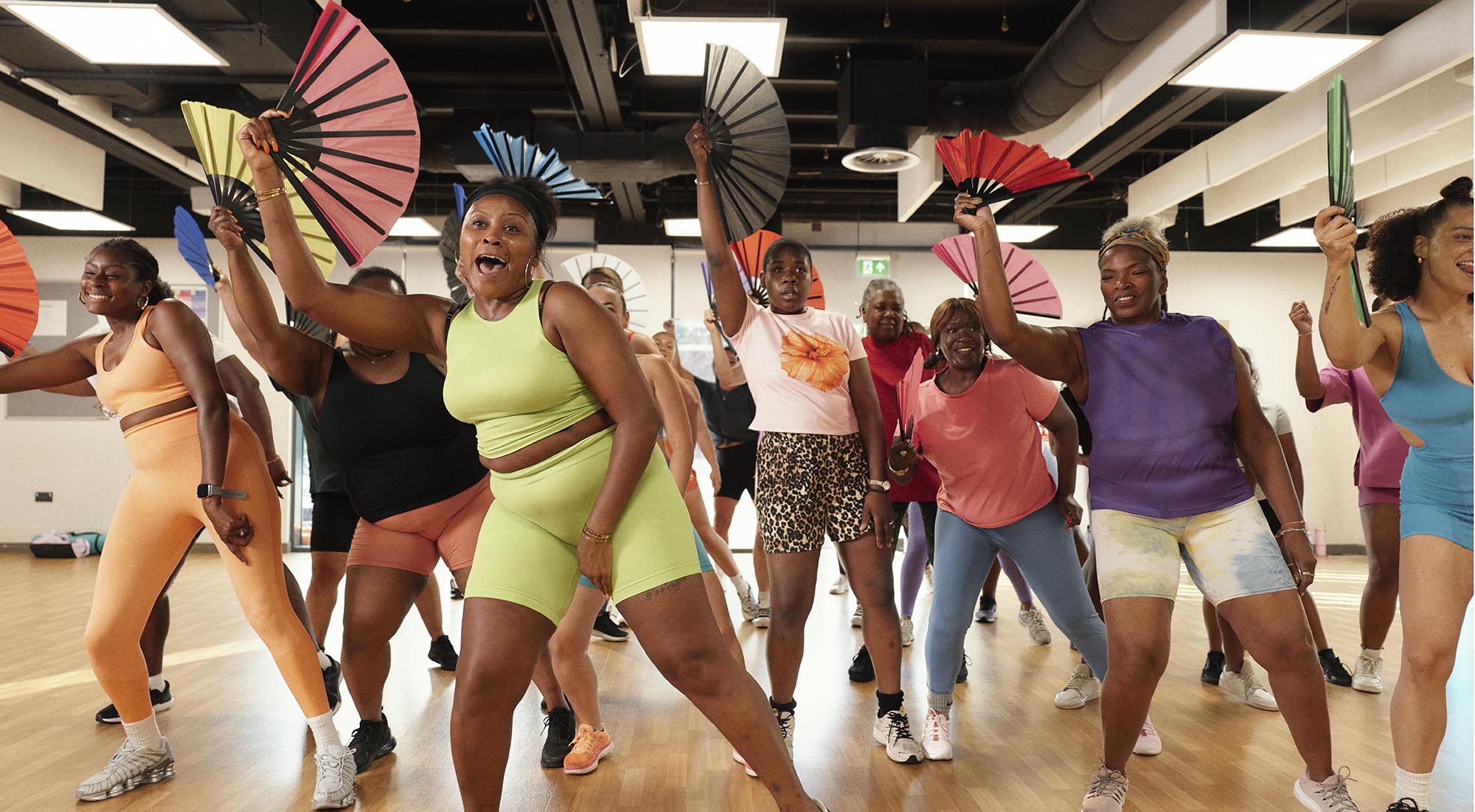 A group of women perform a dance routine in a class, holding and waving paper fans