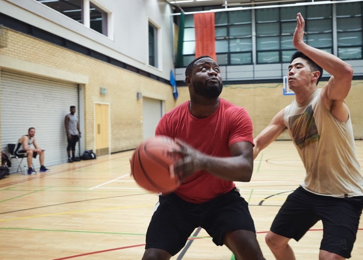 A male basketball player looks to block his opponent from taking a shot on an indoor court.