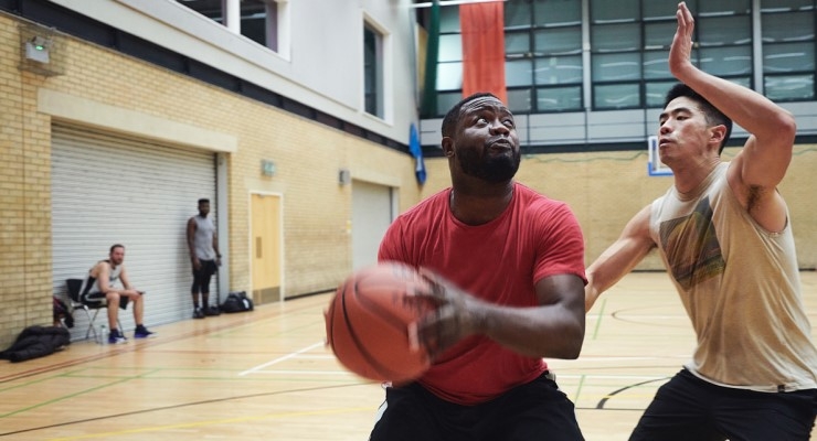 A male basketball player looks to block his opponent from taking a shot on an indoor court.