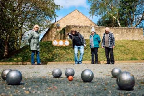 A woman throws a ball during a game of petanque, while three fellow players watch on.