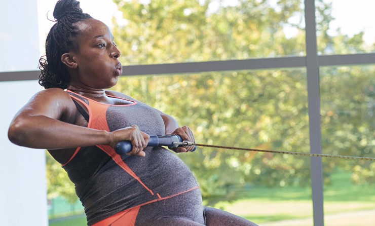 A pregnant woman works out on a rowing machine.