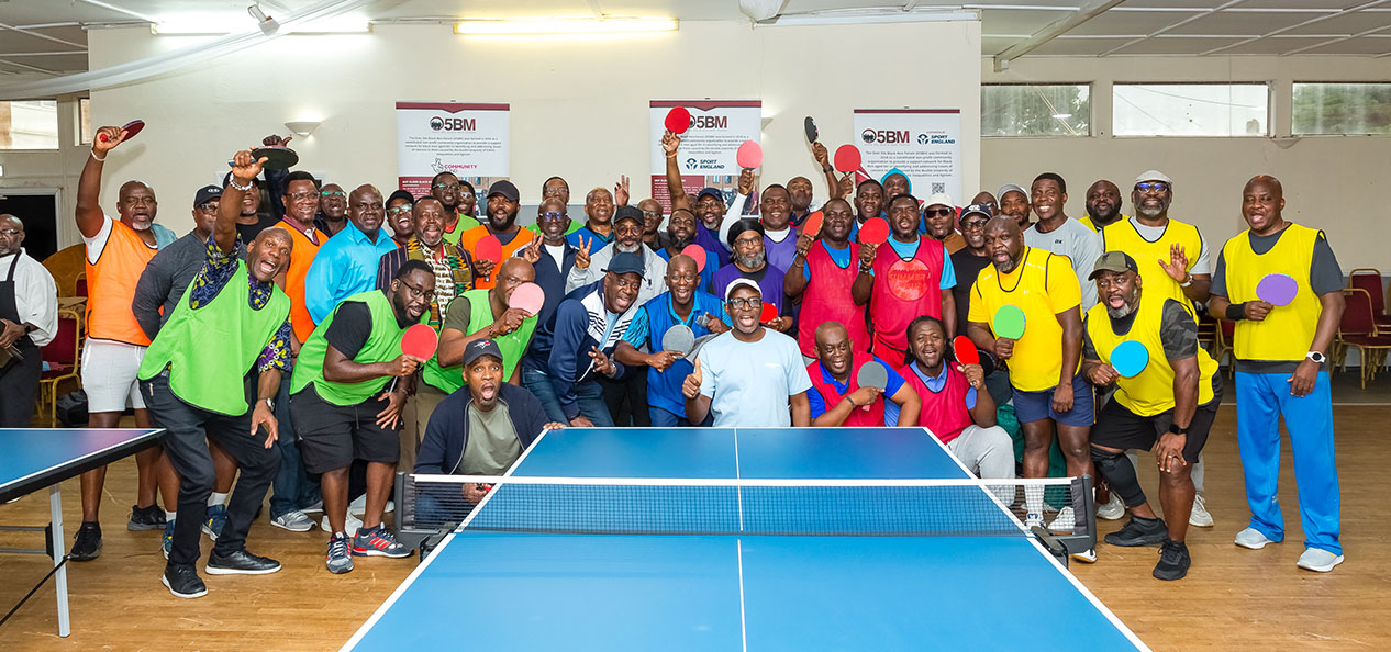 A group of Black men pose during an Over 50s Black Men Forum Table Tennis session on an indoors centre.