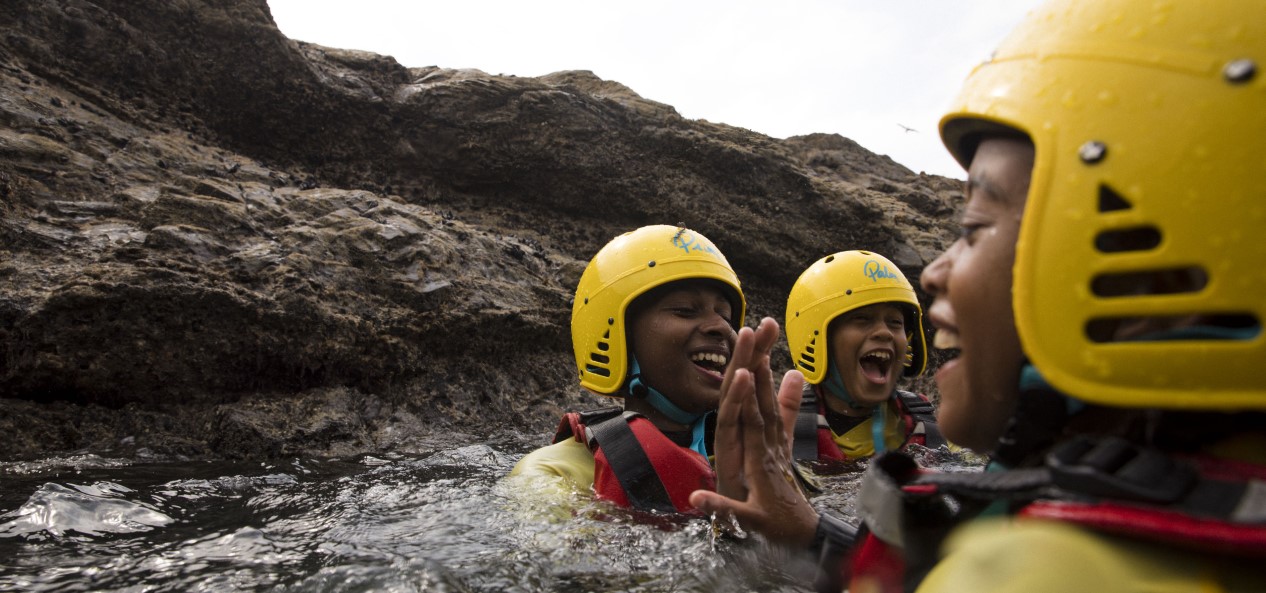 Three young people wearing helmets and buoyancy aids enjoy swimming in the sea.