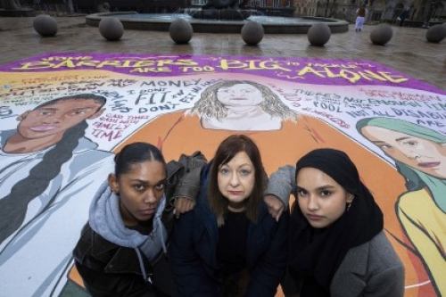 Three women stand on a giant mural featuring illustrations of women and the text 'Some barriers are too big to tackle alone'.