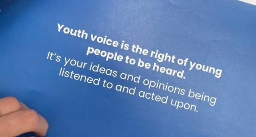 A hand rests on the cover of a document containing the following text: 'Youth voice is the right of young people to be heard. It's your ideas being listened to and acted upon.'