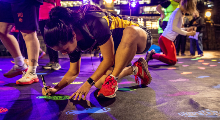 A runner writes on a glow-in-the-dark footprint sticker on the ground.