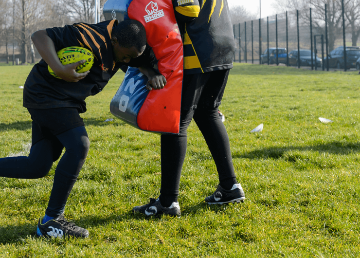 Young boy practicing American Football tackles using a cushion.